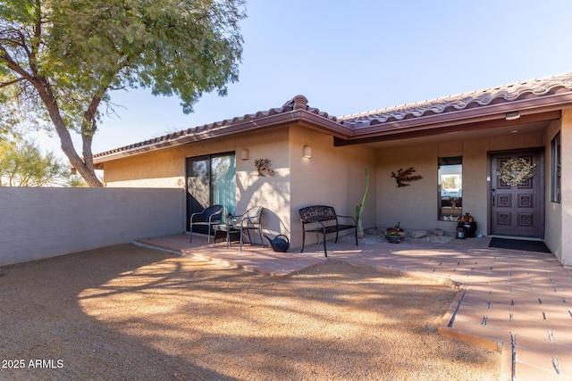 view of exterior entry featuring a tile roof, fence, a patio, and stucco siding