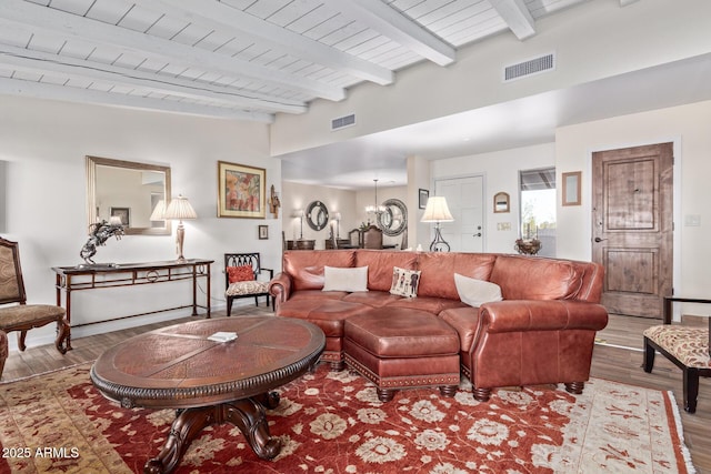 living area featuring lofted ceiling with beams, wood finished floors, visible vents, and a notable chandelier