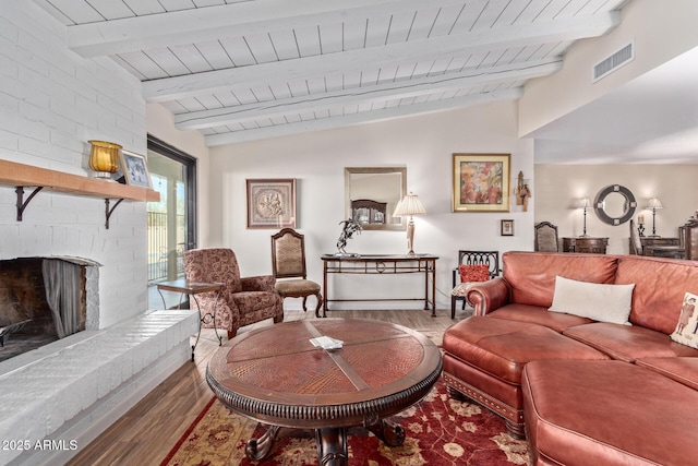 living area with visible vents, wooden ceiling, wood finished floors, vaulted ceiling with beams, and a brick fireplace