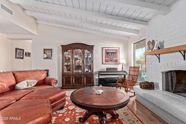 living room with vaulted ceiling with beams, a brick fireplace, visible vents, and wood finished floors