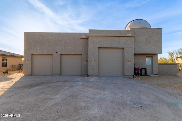 view of front of home with a garage, dirt driveway, and stucco siding