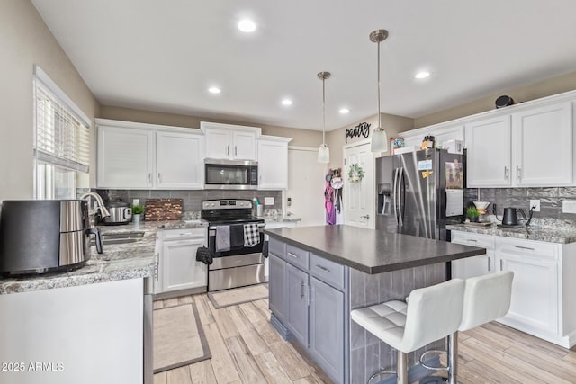 kitchen featuring pendant lighting, sink, stainless steel appliances, a center island, and white cabinets