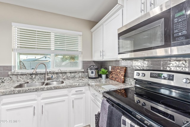 kitchen with sink, appliances with stainless steel finishes, white cabinetry, backsplash, and light stone counters