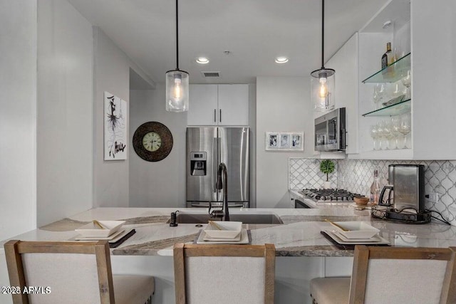 kitchen featuring appliances with stainless steel finishes, white cabinetry, pendant lighting, and decorative backsplash