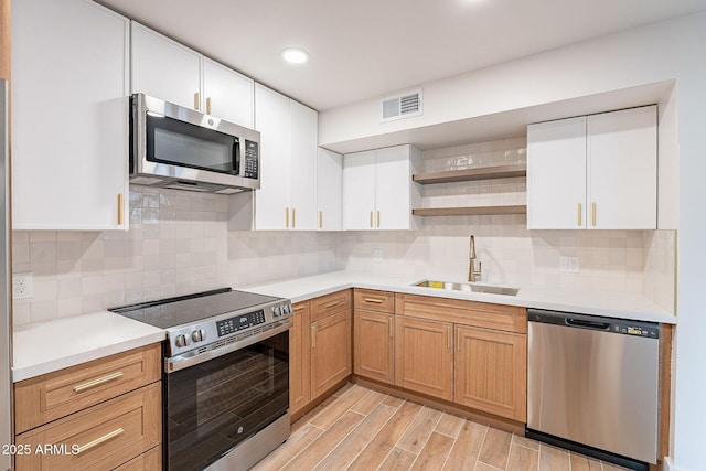 kitchen with appliances with stainless steel finishes, light hardwood / wood-style floors, sink, and white cabinets