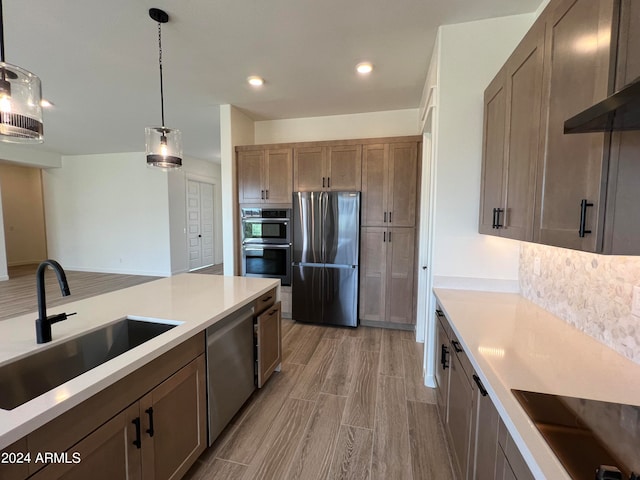 kitchen featuring decorative light fixtures, wood-type flooring, backsplash, sink, and appliances with stainless steel finishes