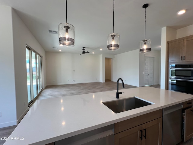 kitchen with decorative light fixtures, a center island with sink, light wood-type flooring, sink, and stainless steel double oven