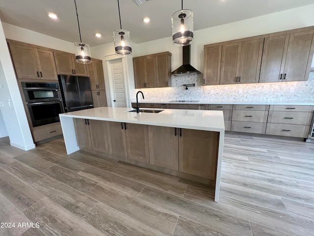 kitchen featuring black appliances, backsplash, wall chimney range hood, sink, and a kitchen island with sink