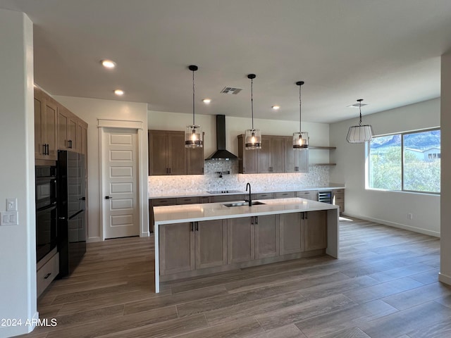 kitchen featuring hanging light fixtures, hardwood / wood-style floors, backsplash, wall chimney range hood, and a kitchen island with sink