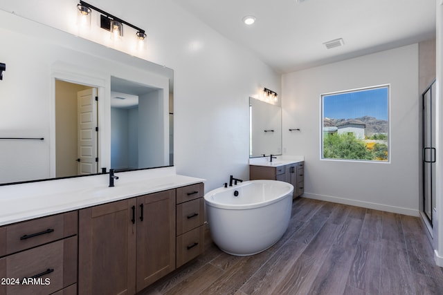 bathroom featuring a tub, vanity with extensive cabinet space, double sink, and wood-type flooring