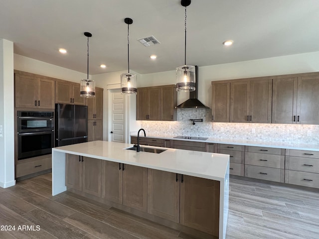 kitchen featuring wall chimney range hood, backsplash, hanging light fixtures, black appliances, and sink