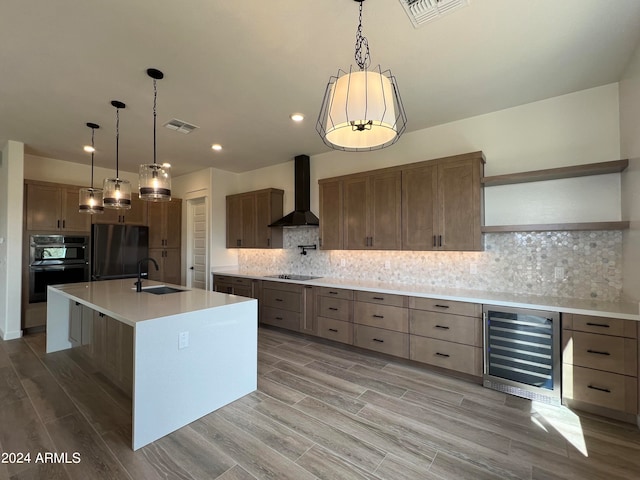 kitchen with a center island with sink, tasteful backsplash, wine cooler, black appliances, and wall chimney exhaust hood