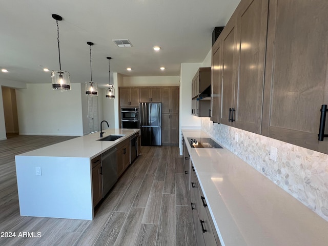 kitchen with wall chimney range hood, light hardwood / wood-style floors, black appliances, an island with sink, and sink