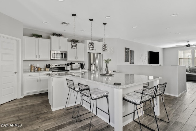 kitchen with an island with sink, hanging light fixtures, white cabinetry, appliances with stainless steel finishes, and a kitchen bar