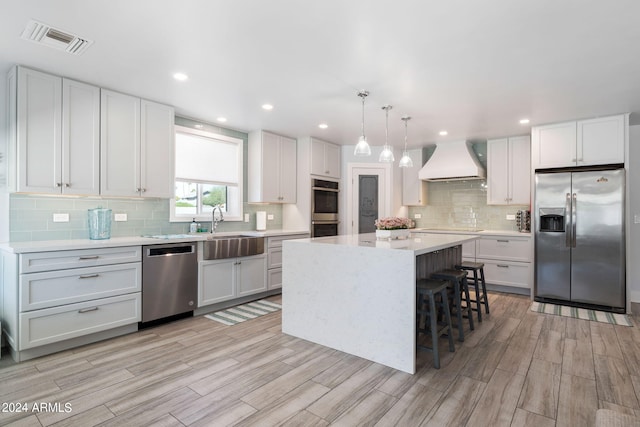 kitchen with a kitchen island, light wood-type flooring, stainless steel appliances, custom range hood, and pendant lighting