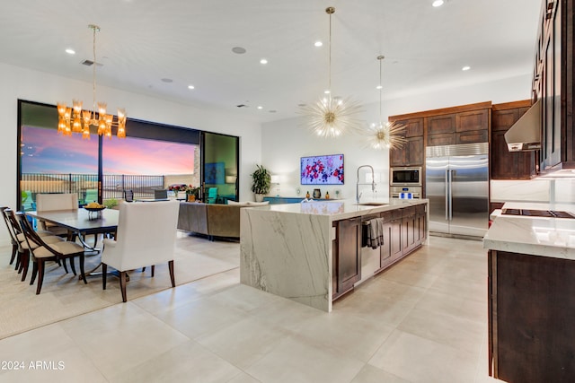 kitchen with pendant lighting, built in appliances, light stone countertops, and a notable chandelier