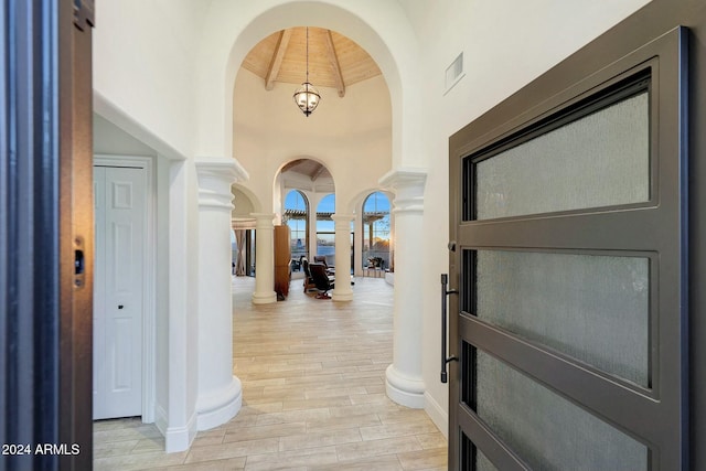 corridor with ornate columns, lofted ceiling with beams, wooden ceiling, and a notable chandelier