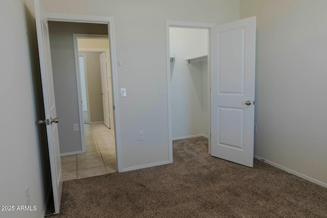unfurnished bedroom featuring baseboards, carpet floors, a spacious closet, and tile patterned flooring