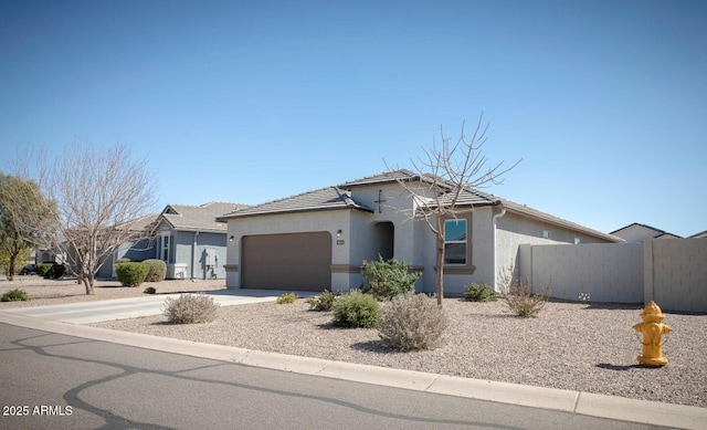 view of front facade with fence, concrete driveway, a tile roof, stucco siding, and an attached garage