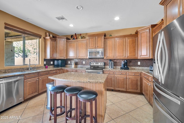 11965 W Monte Vista Rd, Avondale, AZ 85392 - kitchen featuring appliances with stainless steel finishes, light tile patterned flooring, brown cabinetry, a breakfast bar, and recessed lighting