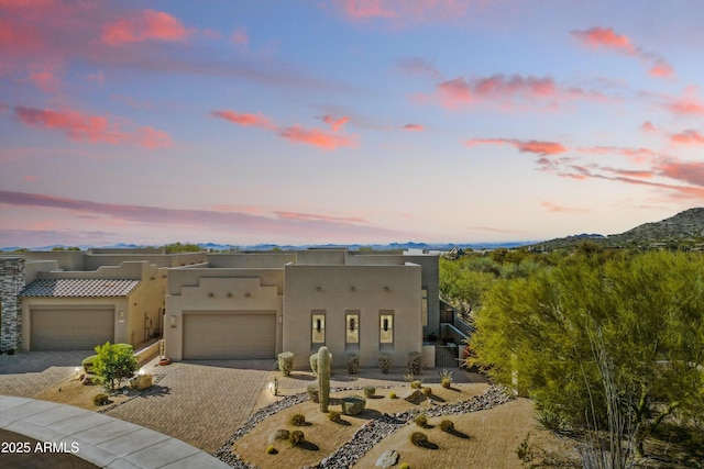 pueblo revival-style home with decorative driveway, stucco siding, an attached garage, and a mountain view