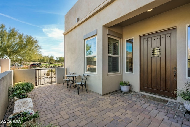 entrance to property featuring stucco siding, fence, and a patio