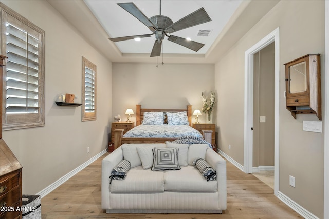 bedroom with a raised ceiling, baseboards, light wood finished floors, and visible vents