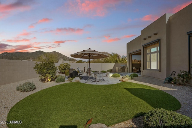 yard at dusk with a patio, a mountain view, and a fenced backyard