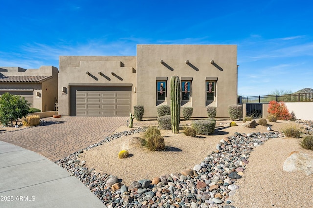 pueblo-style house with stucco siding, driveway, a garage, and fence