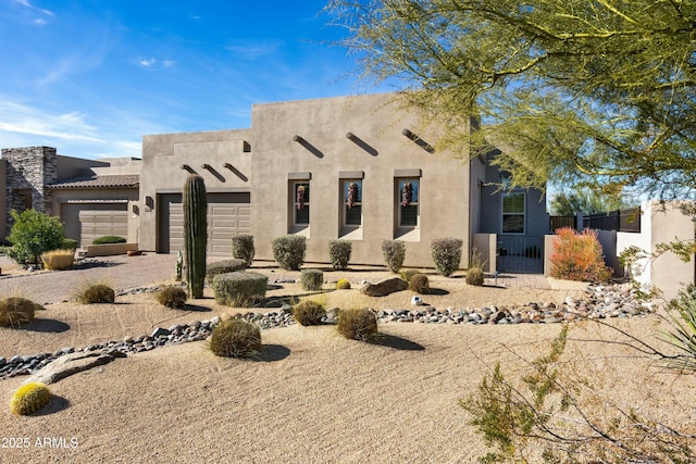 pueblo revival-style home featuring fence, decorative driveway, an attached garage, and stucco siding