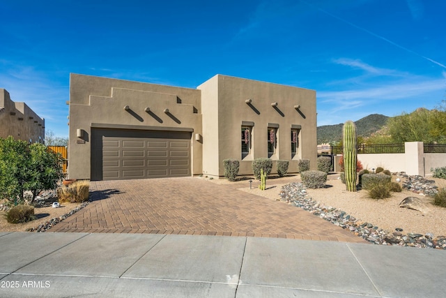 pueblo-style home with stucco siding, fence, decorative driveway, a garage, and a mountain view