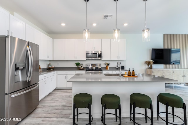 kitchen featuring appliances with stainless steel finishes, a breakfast bar, decorative light fixtures, white cabinetry, and sink