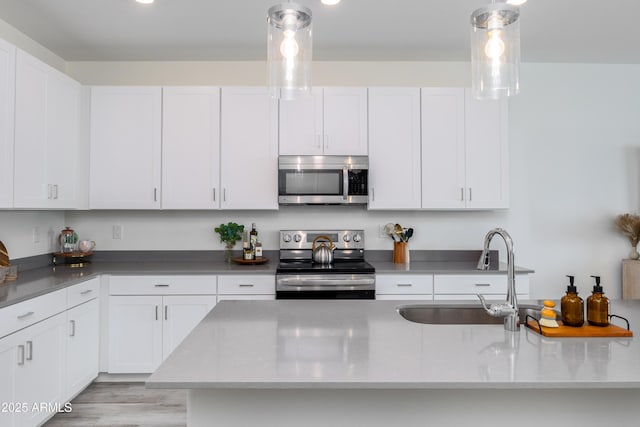 kitchen with pendant lighting, appliances with stainless steel finishes, sink, and white cabinets