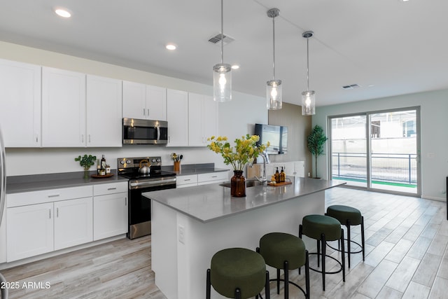 kitchen with pendant lighting, appliances with stainless steel finishes, a kitchen island with sink, and white cabinets