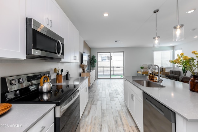 kitchen with appliances with stainless steel finishes, pendant lighting, sink, white cabinets, and a healthy amount of sunlight