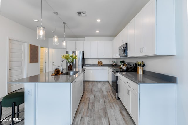 kitchen with white cabinetry, appliances with stainless steel finishes, a kitchen island with sink, and sink