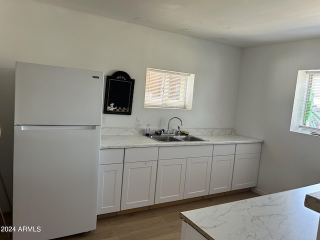 kitchen with light wood-style flooring, white cabinetry, freestanding refrigerator, and a sink