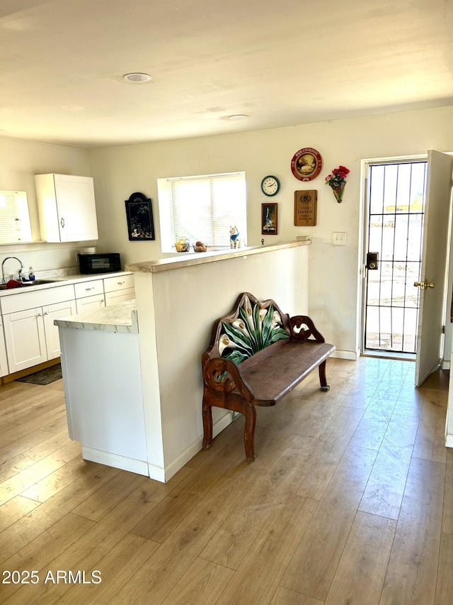 kitchen with baseboards, a sink, light countertops, white cabinets, and light wood-style floors