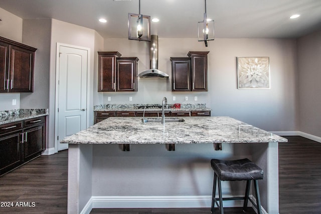 kitchen with dark wood-style flooring, a center island with sink, a sink, wall chimney range hood, and a kitchen breakfast bar