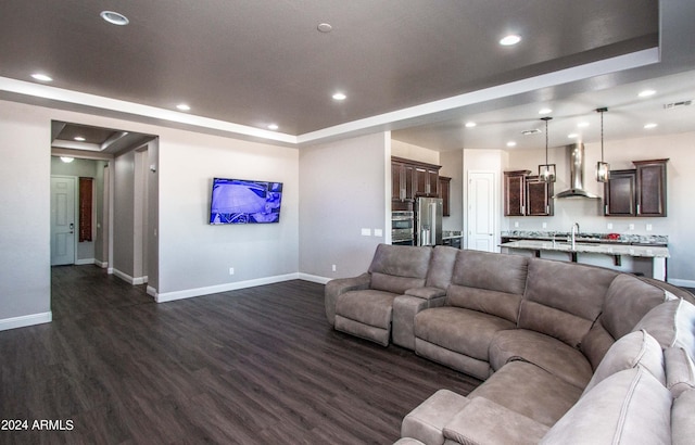 living area with dark wood-style floors, a tray ceiling, baseboards, and recessed lighting