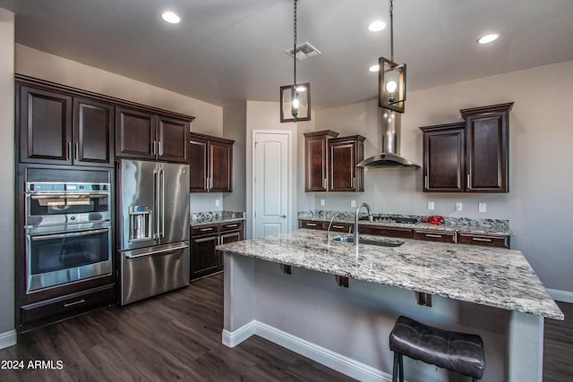 kitchen with wall chimney exhaust hood, stainless steel appliances, dark wood finished floors, dark brown cabinetry, and a sink