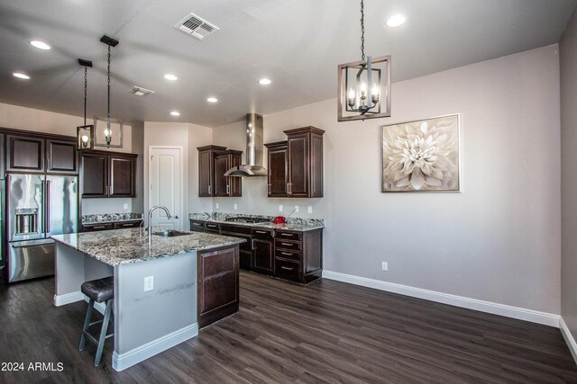 kitchen with appliances with stainless steel finishes, wall chimney exhaust hood, decorative light fixtures, a center island with sink, and dark hardwood / wood-style floors