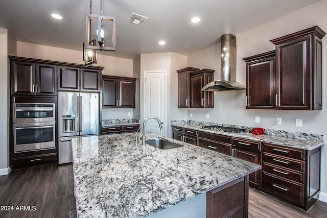 kitchen with light stone counters, a sink, wall chimney exhaust hood, stainless steel appliances, and dark wood-type flooring