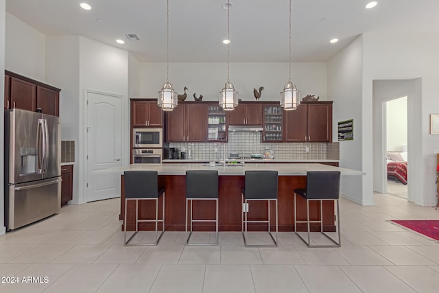 kitchen featuring a towering ceiling, stainless steel appliances, pendant lighting, a center island with sink, and light tile patterned flooring