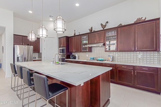 kitchen featuring backsplash, a kitchen island with sink, decorative light fixtures, light tile patterned flooring, and stainless steel appliances