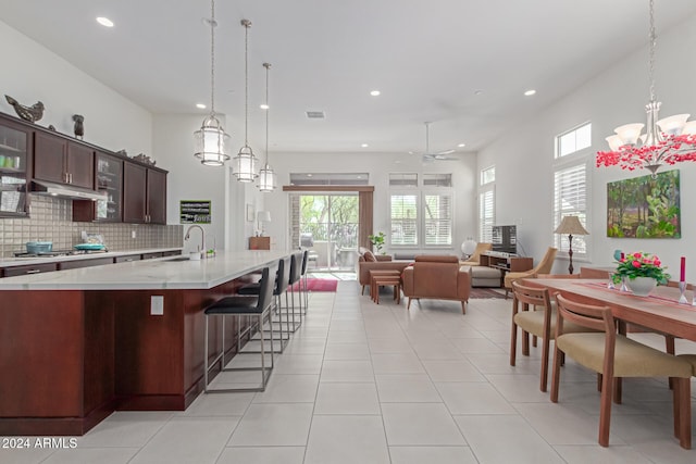 kitchen with ceiling fan with notable chandelier, hanging light fixtures, light tile patterned floors, light stone counters, and dark brown cabinetry