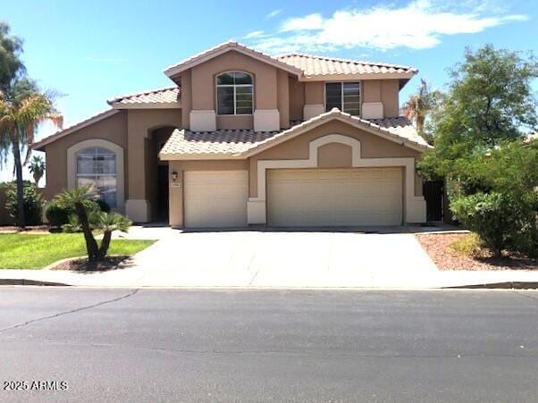 mediterranean / spanish-style home with a tile roof, driveway, an attached garage, and stucco siding