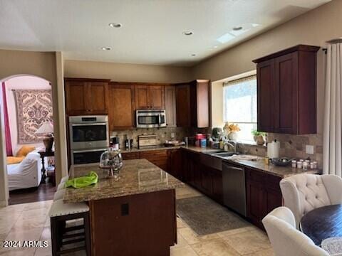 kitchen with appliances with stainless steel finishes, decorative backsplash, a kitchen island, and light stone countertops