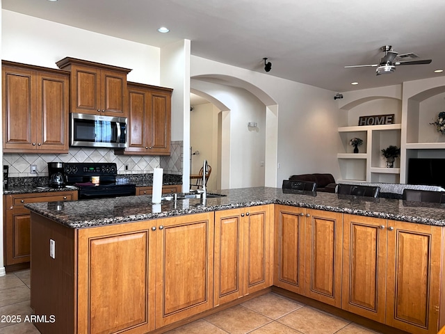 2427 W Desert Hills Estate Dr, Phoenix, AZ 85086 - kitchen with stainless steel microwave, black range with electric cooktop, open floor plan, dark stone countertops, and a sink
