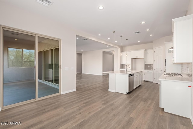 kitchen featuring sink, appliances with stainless steel finishes, white cabinetry, hanging light fixtures, and a center island with sink